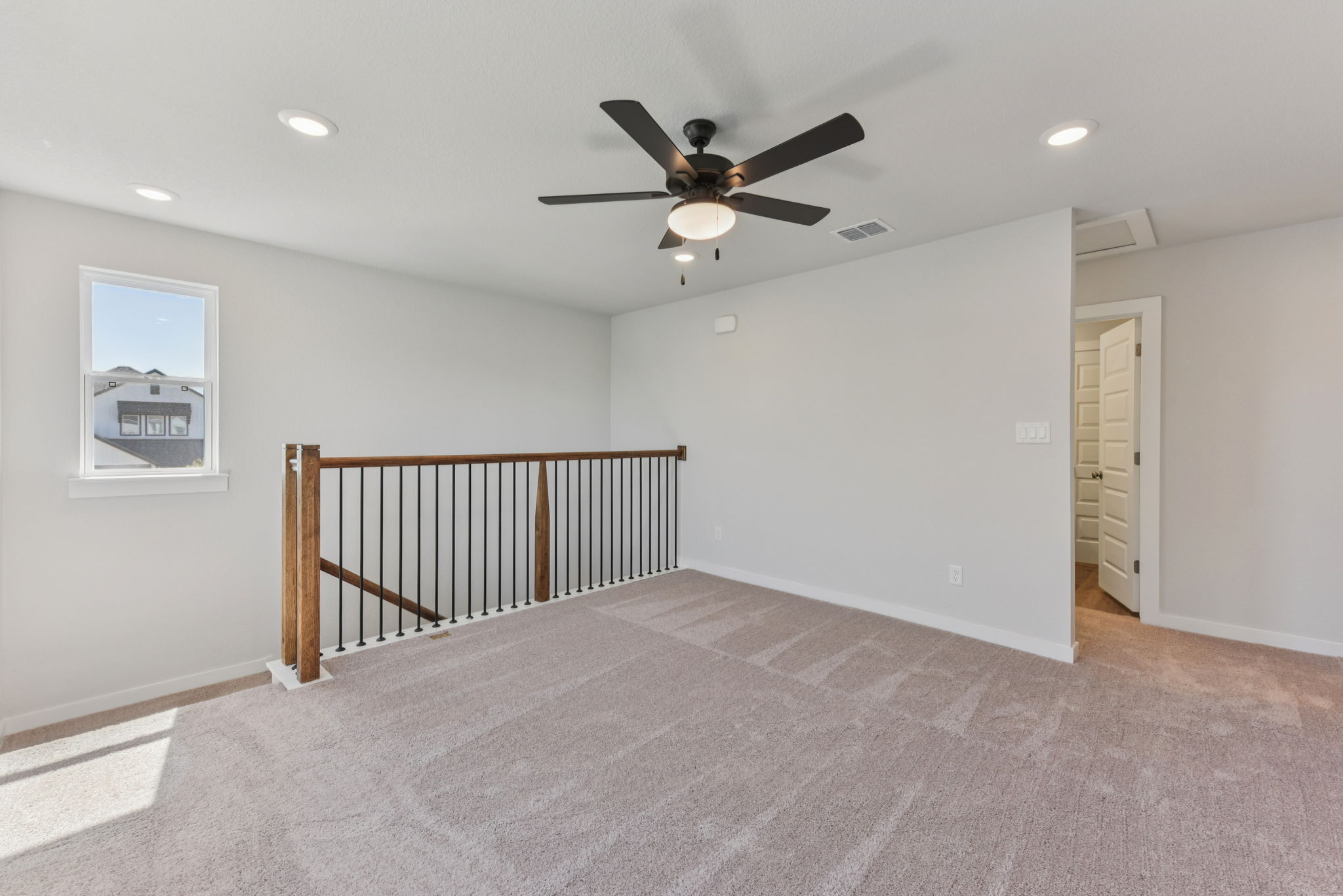 A room with a ceiling fan and a wood railing.