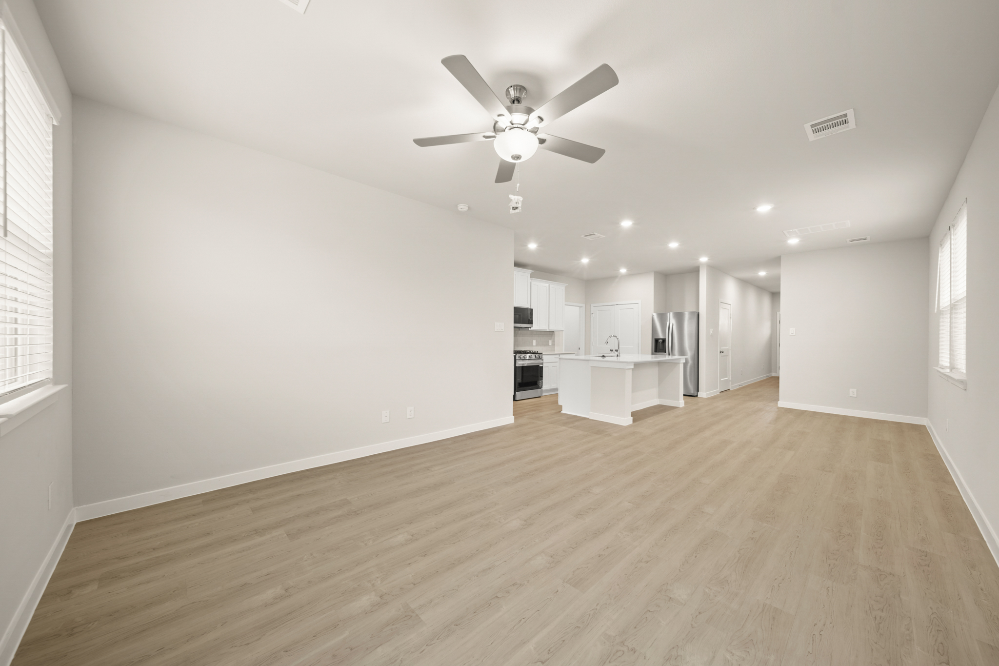 A large empty room with a ceiling fan and a wood floor.