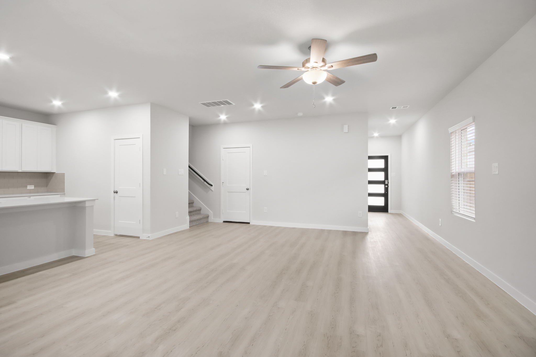 A large empty room with a ceiling fan and white cabinets.