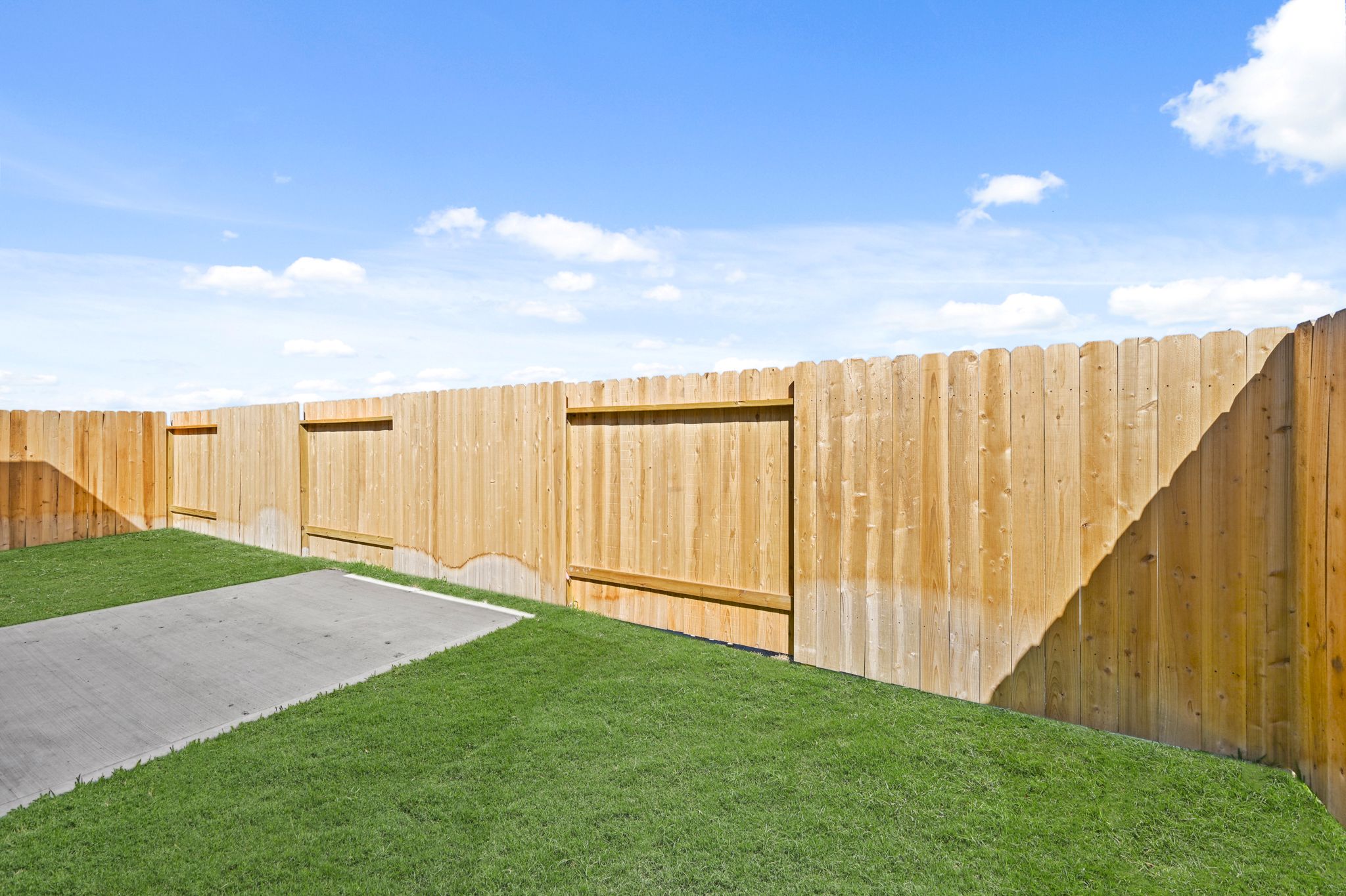 A fenced in area with a green lawn and a path with Nelson-Atkins Museum of Art in the background.